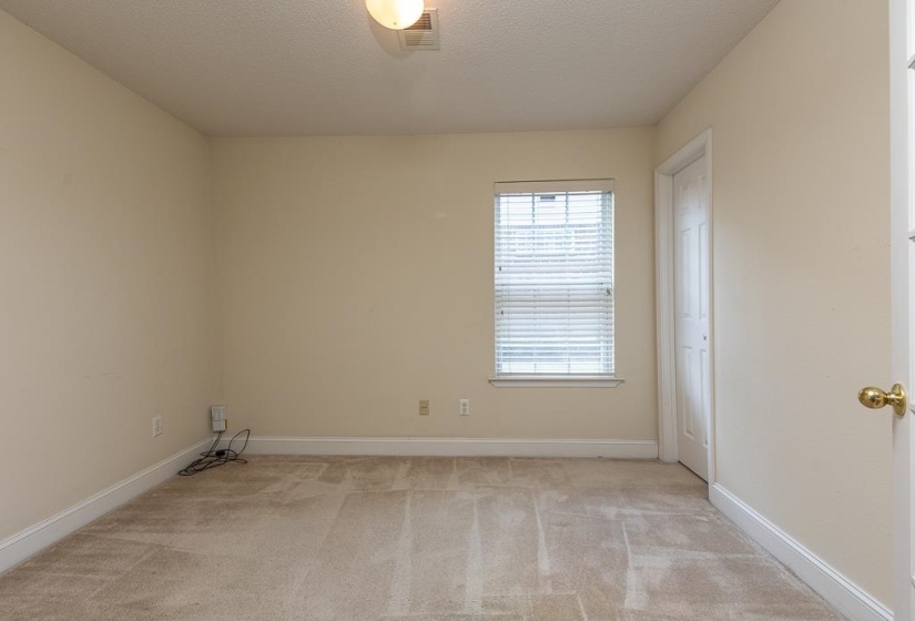 Carpeted room featuring a single window with blinds, a ceiling-mounted light fixture, white trim, and a paneled interior door