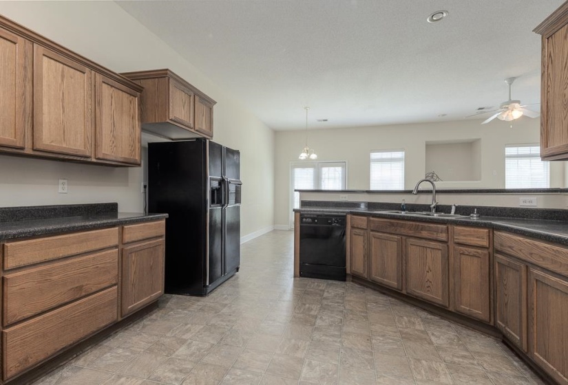 Kitchen featuring extensive wood cabinetry, dark countertops, black appliances, and durable tile flooring