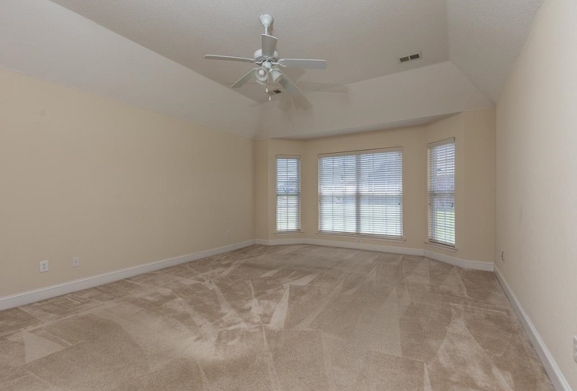 Spacious room featuring a tray ceiling with a ceiling fan, bay windows with blinds, neutral wall tones, and patterned carpeting