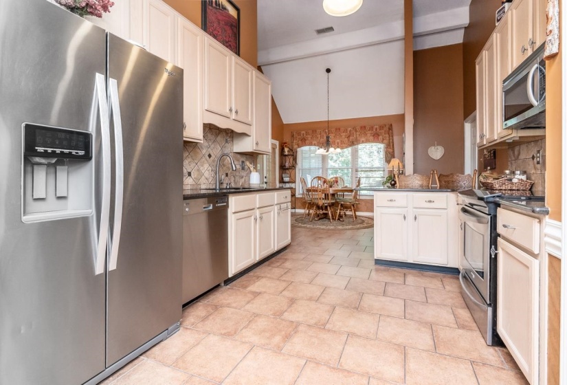 Kitchen featuring stainless steel appliances, light-toned cabinetry, dark countertops, a tiled backsplash, and stone-look tile flooring