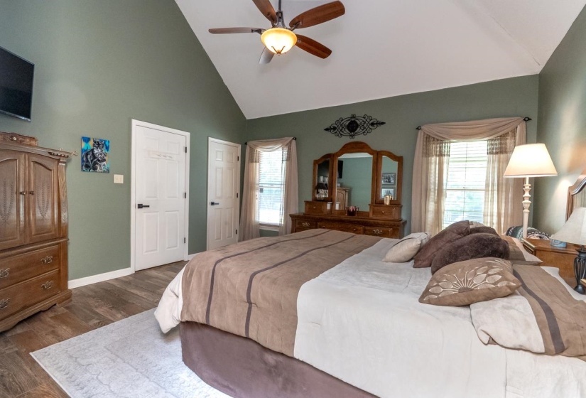 Vaulted ceiling room featuring wood-finish flooring, two panel doors with black hardware, and a window with blinds