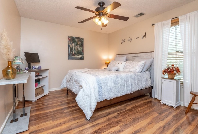 Spacious room featuring wood-finish flooring, a ceiling fan with integrated lighting, and a window with blinds and sheer curtains