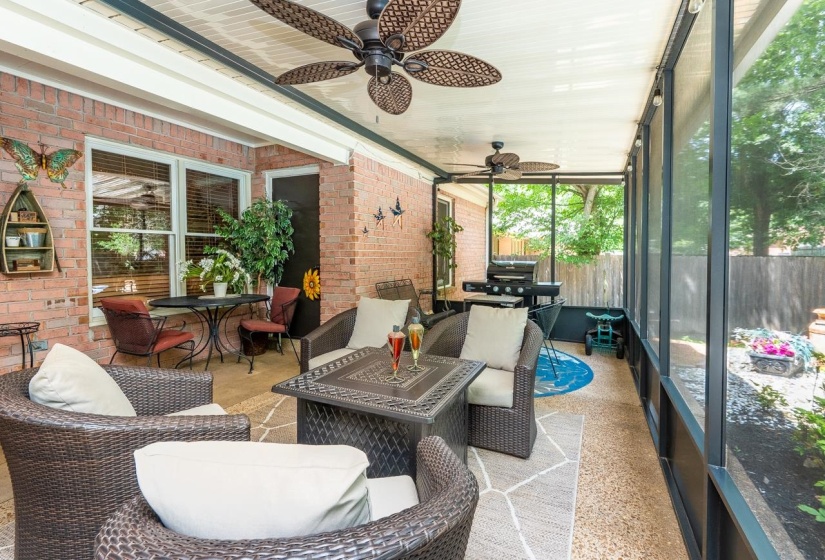 Screened patio featuring a brick exterior wall, dual ceiling fans, exposed aggregate flooring, and a fenced perimeter