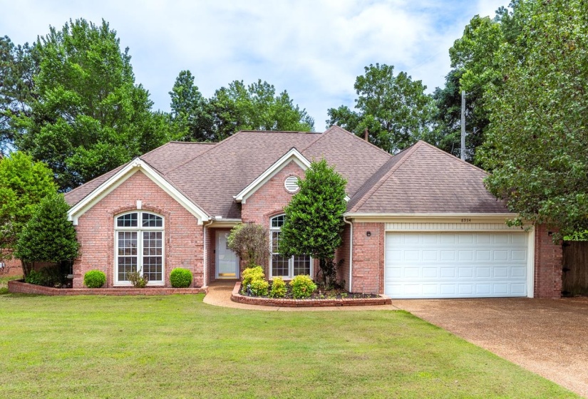 Brick exterior with arched windows, a front-facing garage, and mature landscaping