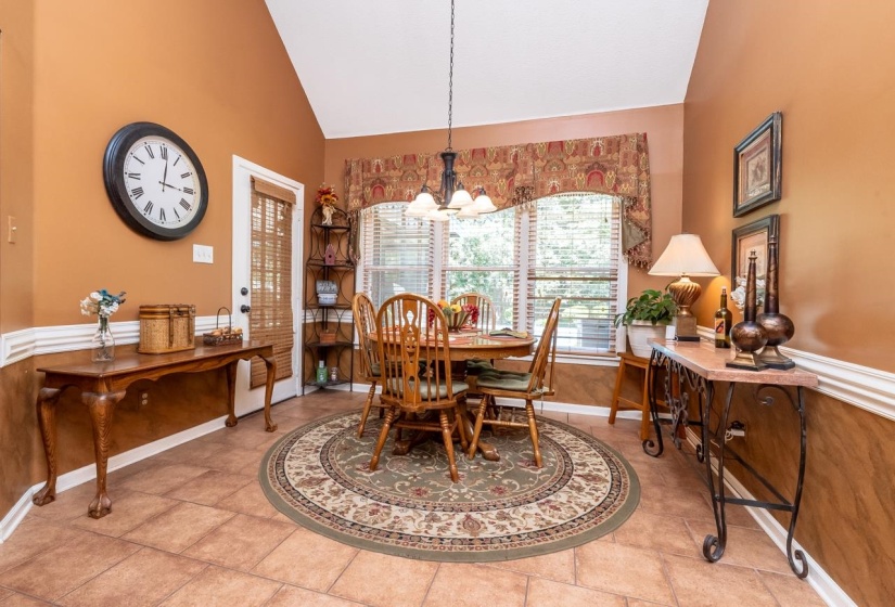 Eat-in. kitchen featuring vaulted ceilings, windows with blinds, a multi-light chandelier, tile flooring, and chair rail molding