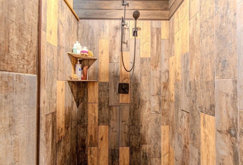 Shower enclosure featuring vertical wood-look tile, a matte black shower head, coordinating control lever, and a built-in corner shelf