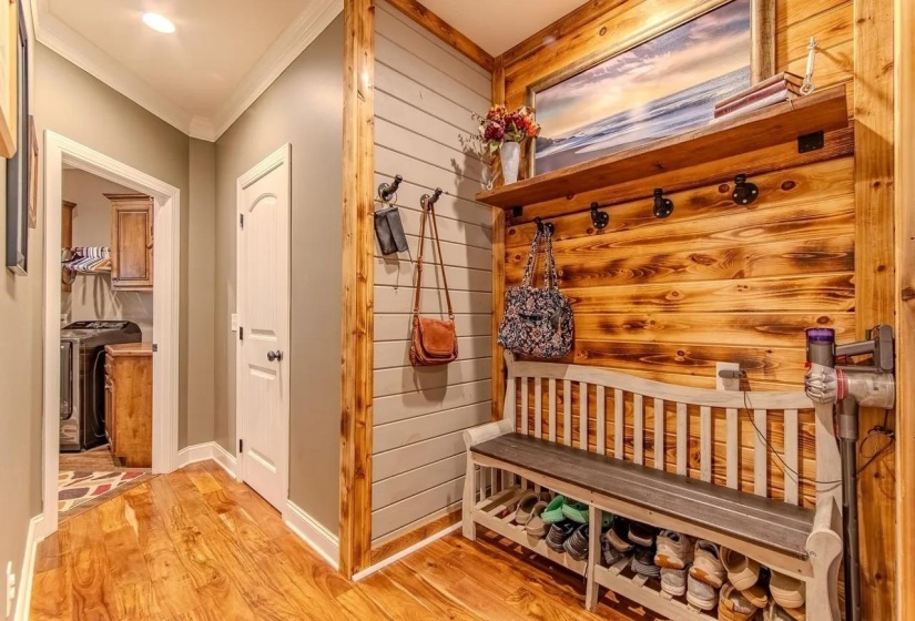 Hallway featuring wood-finish flooring, a wood accent wall with a built-in shelf, and a built-in bench with shoe storage