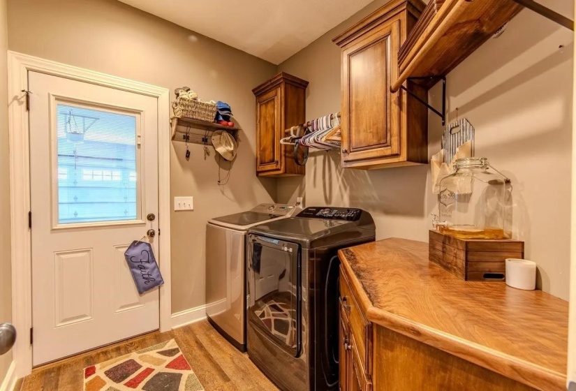Laundry room featuring wood-finish flooring, overhead cabinetry, and a countertop with natural wood grain
