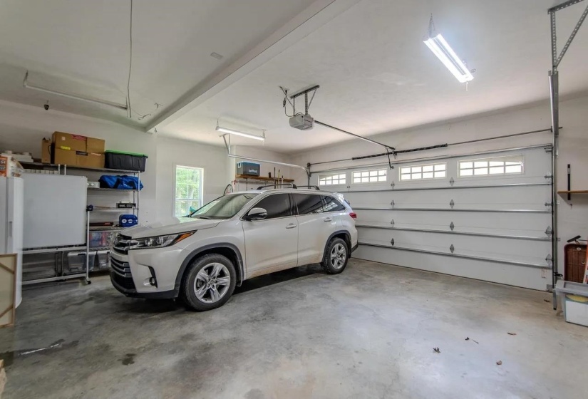 Spacious garage featuring a concrete floor, overhead lighting, and a white paneled garage door with upper window inserts