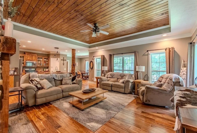 Spacious living area featuring wood-finish flooring, a tray ceiling with wood paneling, and a ceiling fan