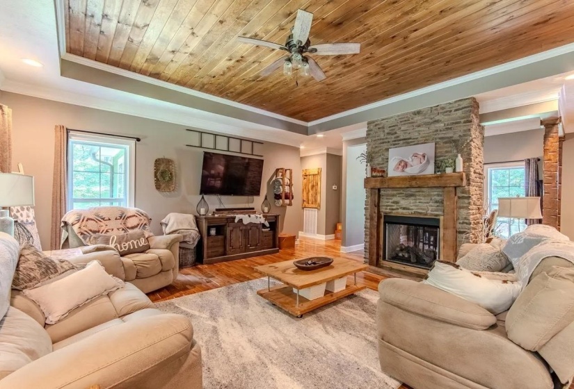 Living area featuring a stone-clad fireplace with a wood mantel, wood-finish flooring, and a wood plank ceiling