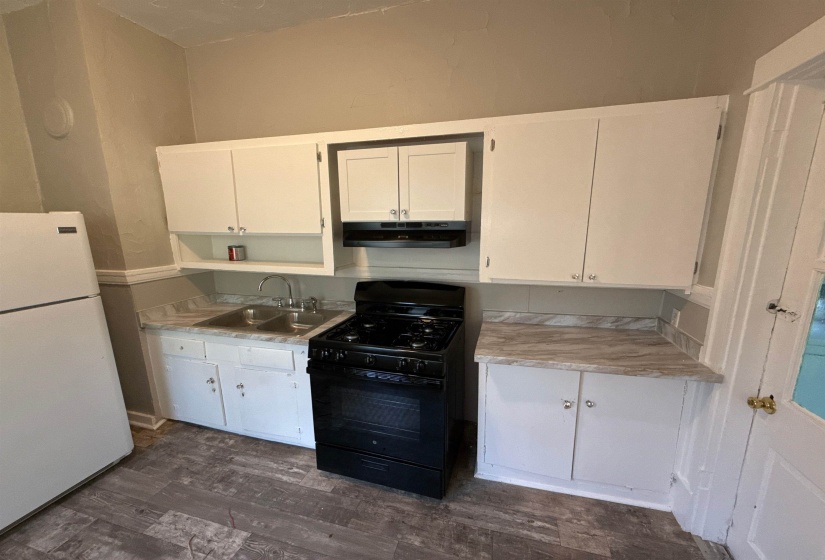 Kitchen with freestanding refrigerator, black gas range, under cabinet range hood, light countertops, and white cabinetry
