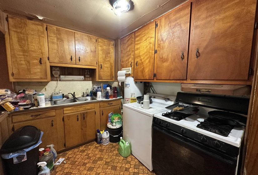 Kitchen featuring wood cabinetry, a double basin stainless steel sink, a gas range with an oven, and patterned flooring