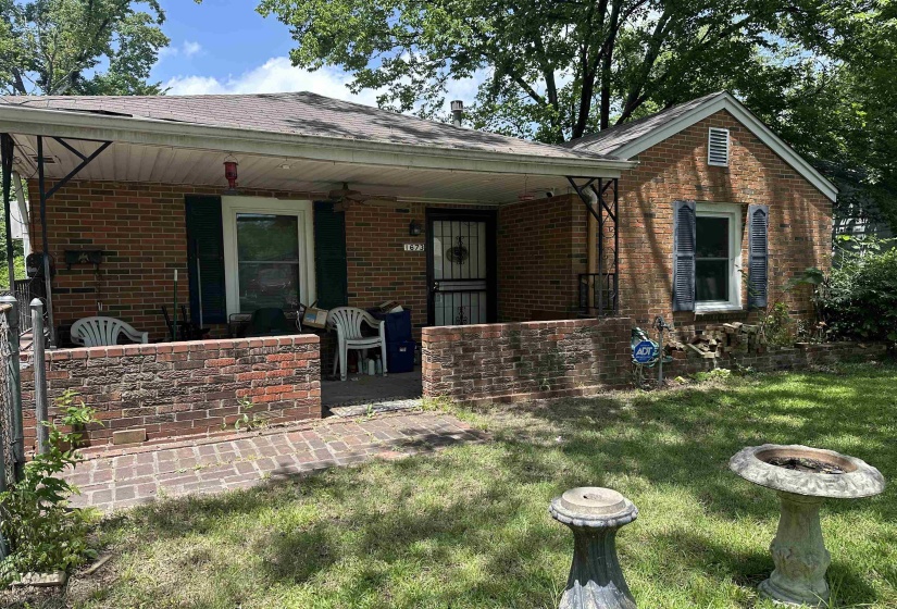 Brick exterior home featuring a covered front porch, brick half-wall, and a brick paver patio