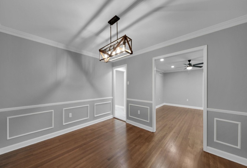 Unfurnished dining area with crown molding, dark wood-style floors, a decorative wall, a ceiling fan, and a chandelier