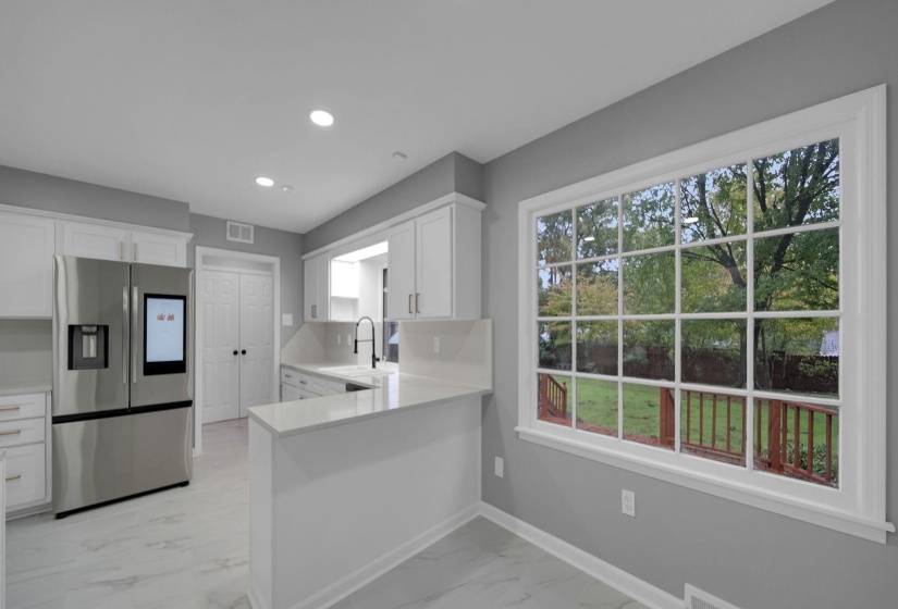 Kitchen featuring stainless steel fridge, white cabinetry, light marble finish flooring, a peninsula, and recessed lighting