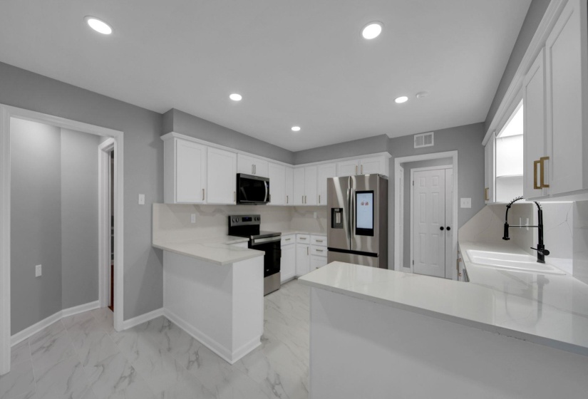 Kitchen with a peninsula, appliances with stainless steel finishes, recessed lighting, white cabinetry, and light marble finish floors