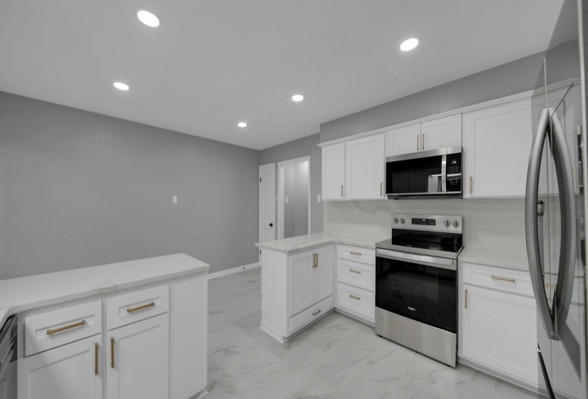Kitchen featuring stainless steel appliances, a peninsula, white cabinetry, recessed lighting, and light marble finish floors