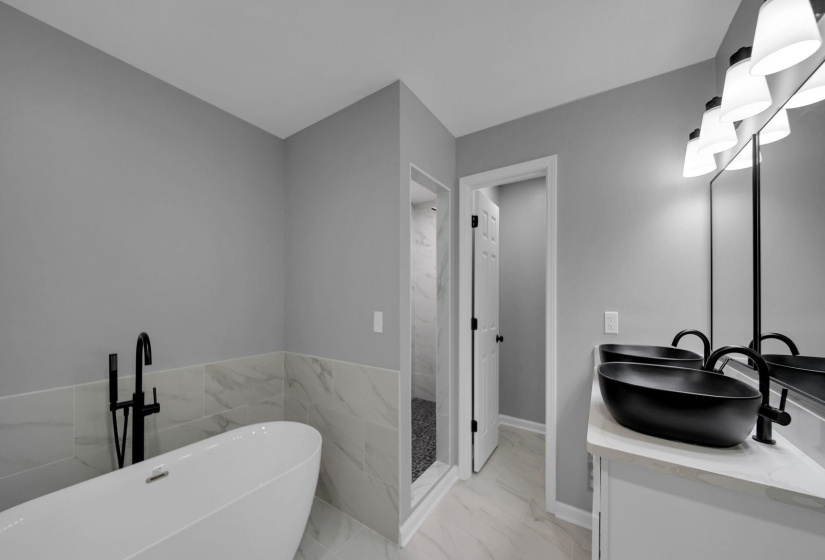 Bathroom featuring a freestanding tub, light marble finish floors, double vanity, and a marble finish shower