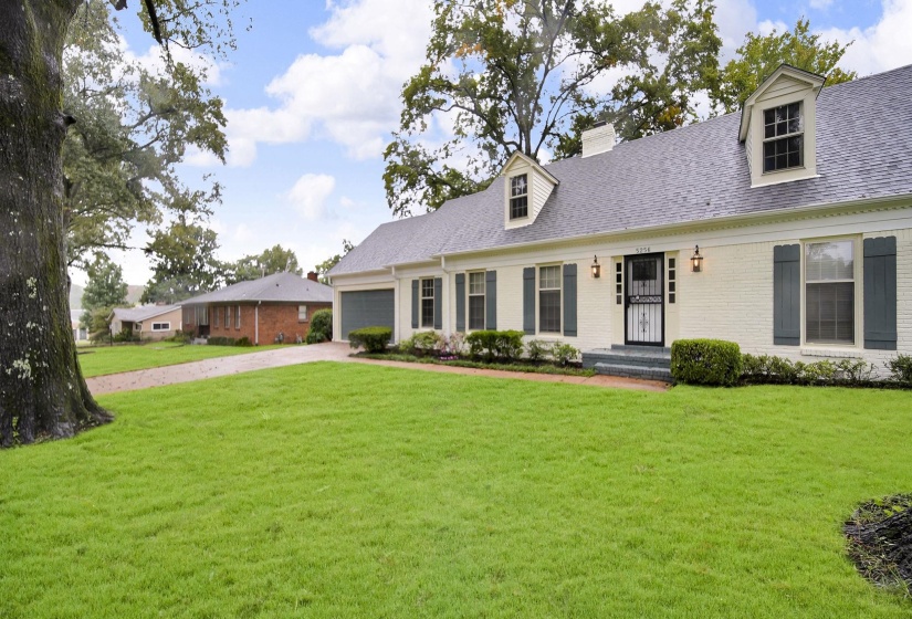New england style home with driveway, a front yard, a shingled roof, a chimney, and brick siding