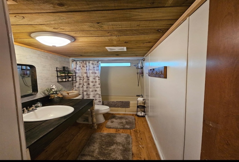 Bathroom featuring a dark wood-finish vanity with a white vessel sink, wood-finish flooring, a neutral-toned bathtub, a flush-mount ceiling light, and a wood-plank ceiling