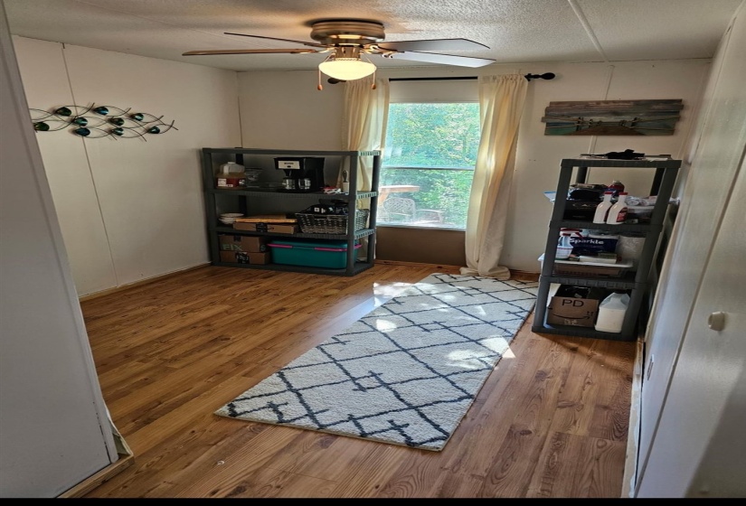 Room featuring wood-finish flooring, a ceiling fan with integrated lighting, and a window with sheer drapes