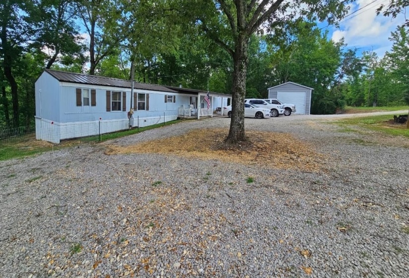 White exterior residence featuring a detached garage, a gravel driveway, and surrounding natural foliage