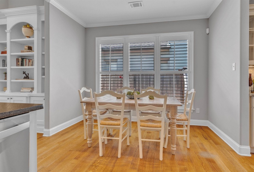Dining area featuring wood-finish flooring, white plantation shutters, built-in shelving, crown molding, and neutral wall tones
