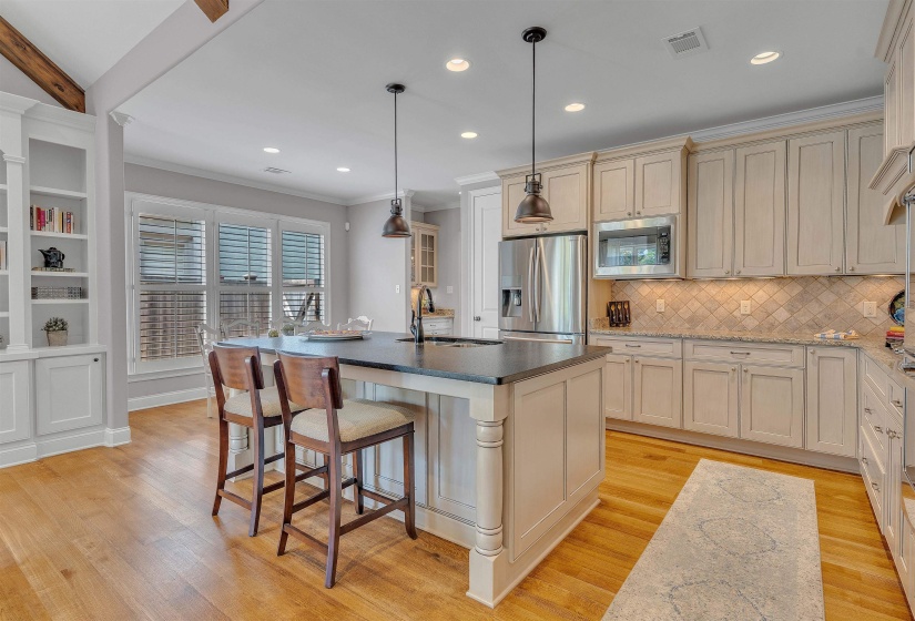 Kitchen featuring a central island with a dark countertop, light-toned cabinetry, stainless steel appliances, a tiled backsplash, and wood-finish flooring