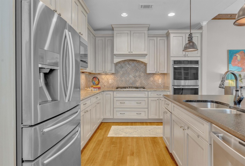 Kitchen featuring stainless steel appliances, light-toned cabinetry, a patterned backsplash, and wood-finish flooring