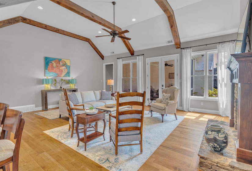 Vaulted ceiling featuring exposed wood beams, a ceiling fan, recessed lighting, wood-finish flooring, and a stone-clad fireplace