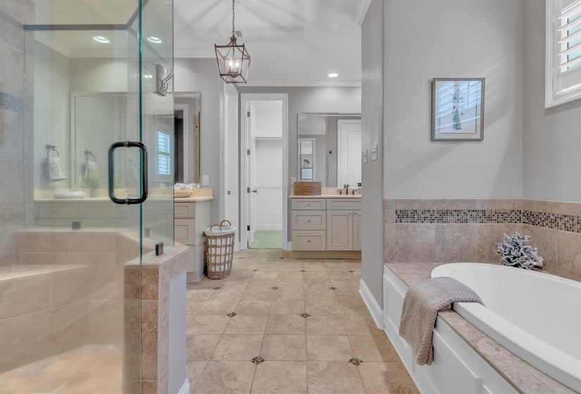 Glass-enclosed shower with tiled bench, freestanding soaking tub with tile surround, and dual vanity areas with integrated sinks