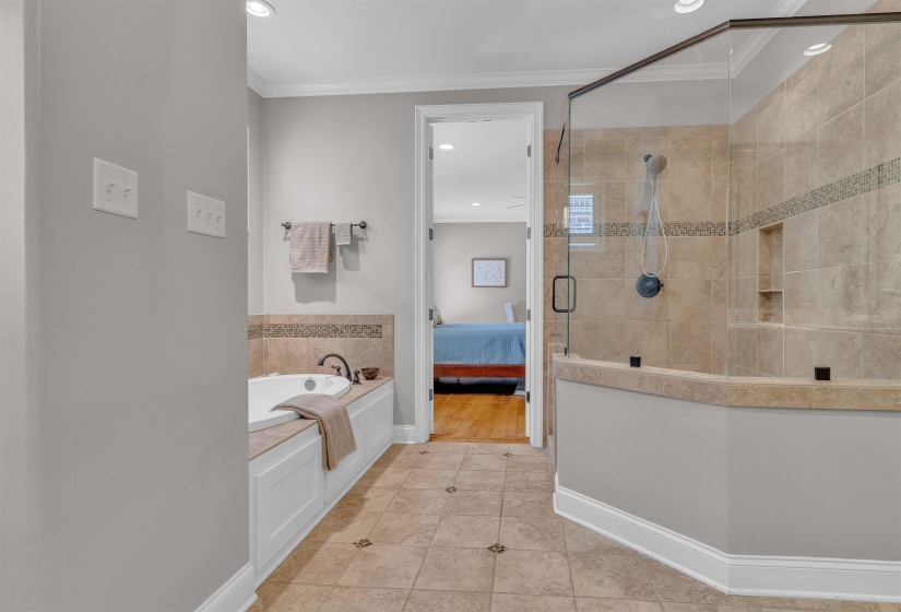 Spacious bathroom featuring a glass-enclosed shower with tiled walls and built-in niche, a white soaking tub with dark bronze fixtures, and large-format floor tiling with decorative inserts