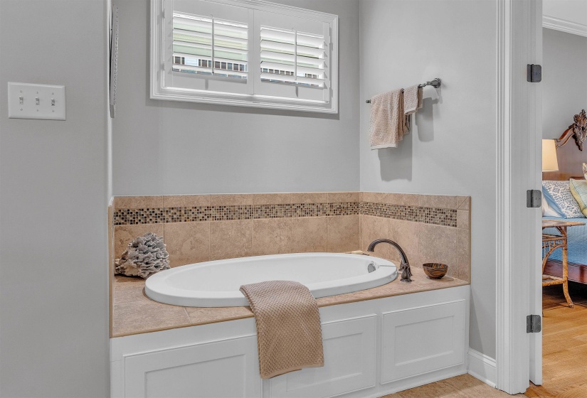 Built-in soaking tub featuring a bronze-finish faucet, surrounded by tiled decking and a mosaic tile accent band