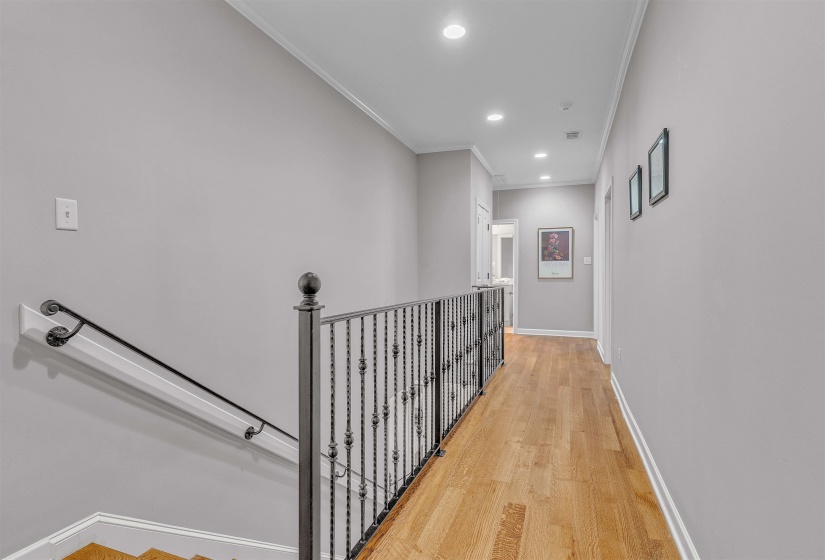 Upper-level hallway featuring wood-finish flooring, recessed lighting, and a decorative wrought iron railing