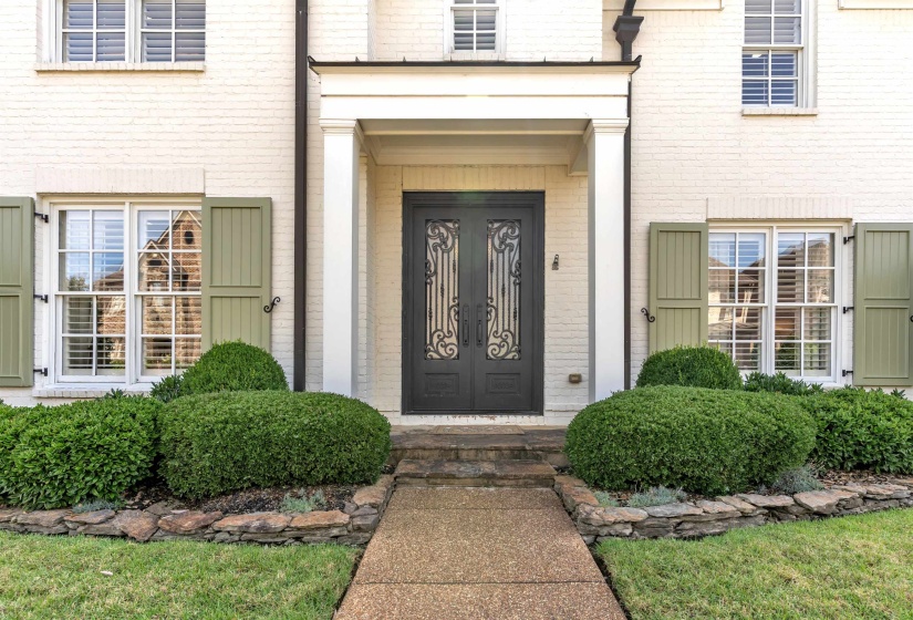 Brick exterior with white paint finish, featuring a double entry door with decorative ironwork, a covered portico, and light green operational shutters on a double-hung window
