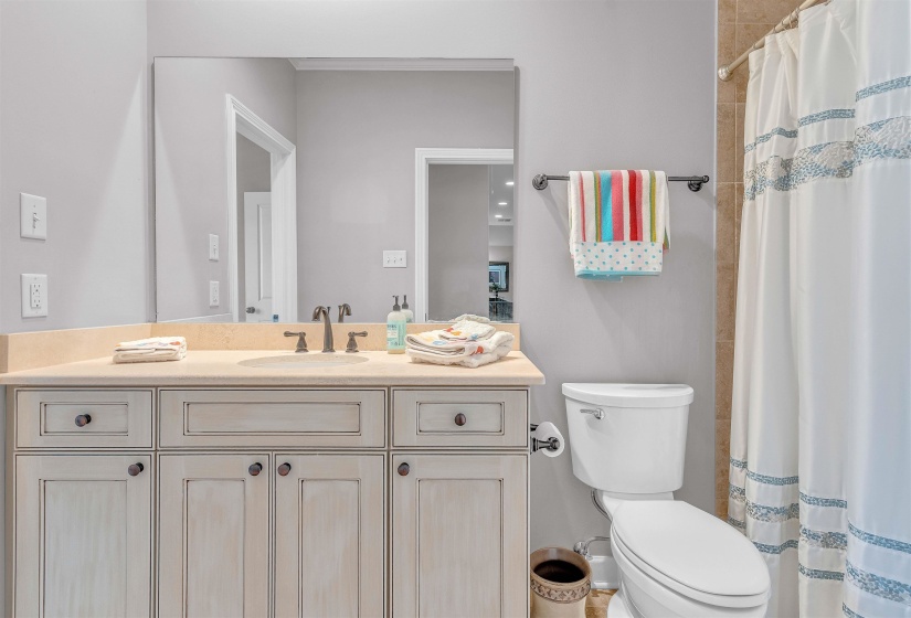 Bathroom featuring a light-toned vanity with a built-in sink, a large wall-mounted mirror, and tile-surround shower area