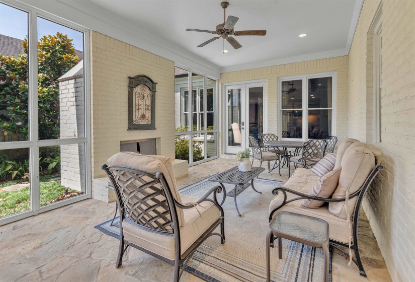 Screened patio featuring natural stone flooring, an integrated fireplace with decorative mantel, white brick walls, a ceiling fan, and access to interior spaces through French doors