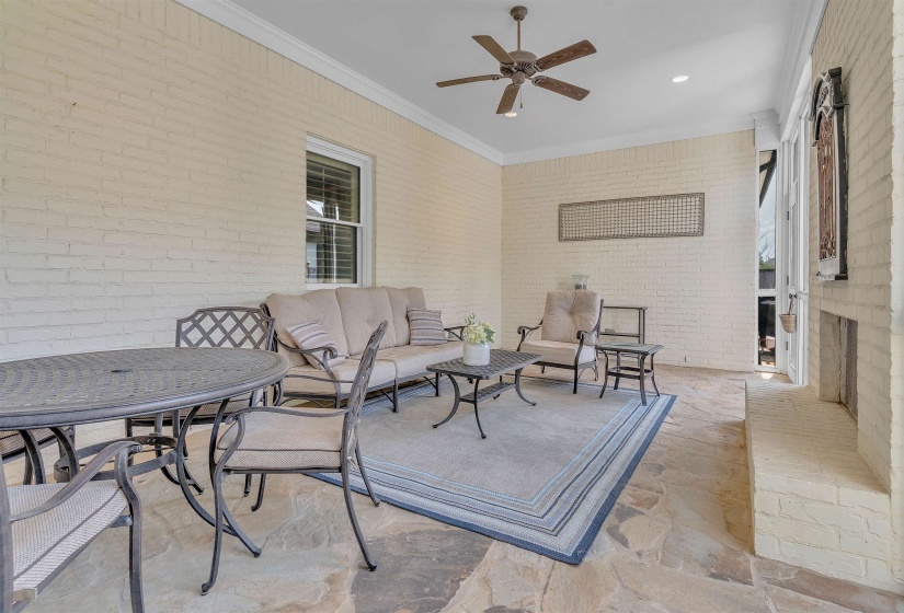 Covered patio featuring flagstone flooring, painted brick walls, a built-in fireplace, and a ceiling fan