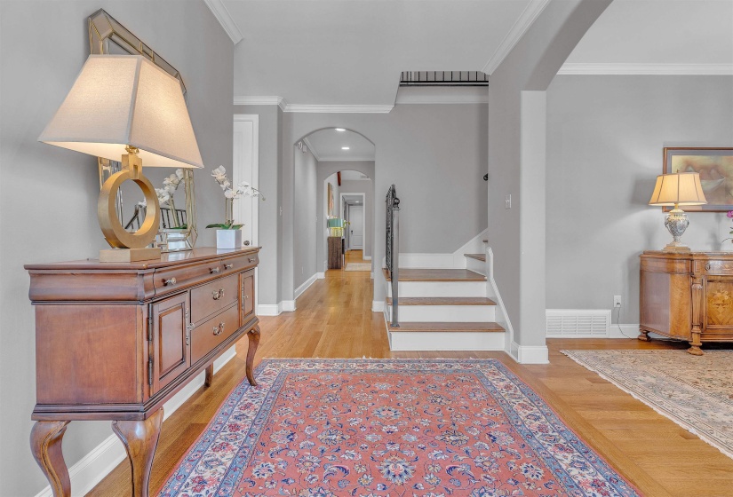 Hardwood flooring throughout the entry, staircase with white risers and dark wood treads, and arched doorways
