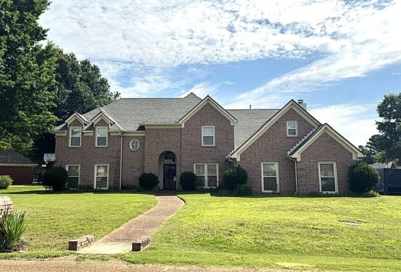 Traditional brick exterior residence featuring a prominent arched entry, multiple dormer windows, a circular window accent, and a gray shingle roof