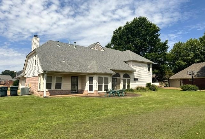 Rear exterior featuring a brick and siding facade, multi-level shingle roof, and a ground-level patio