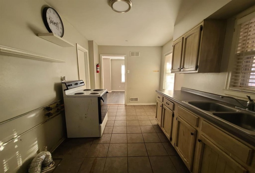 Kitchen featuring tile flooring, wood-finish cabinetry, dual basin sink, window with horizontal blinds, and a white freestanding range