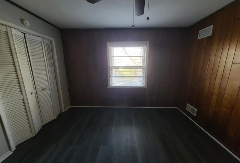 Room featuring dark wood-finish flooring, a window with blinds, and paneled walls