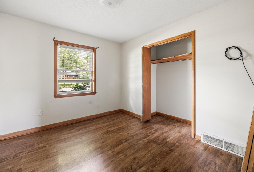 Room featuring wood-finish flooring, a window with horizontal blinds, and a built-in closet with wood trim