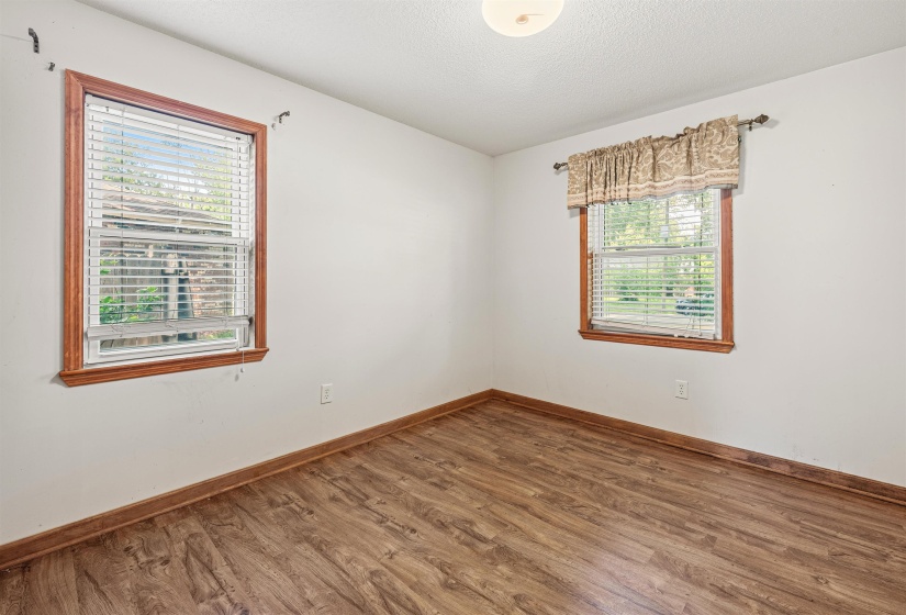 Room featuring wood-finish flooring, two windows with wood trim, white walls, and a ceiling-mounted light fixture