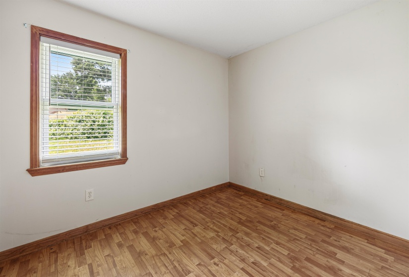 Room with light-toned wall finishes, wood-finish flooring, and a single window featuring wood trim