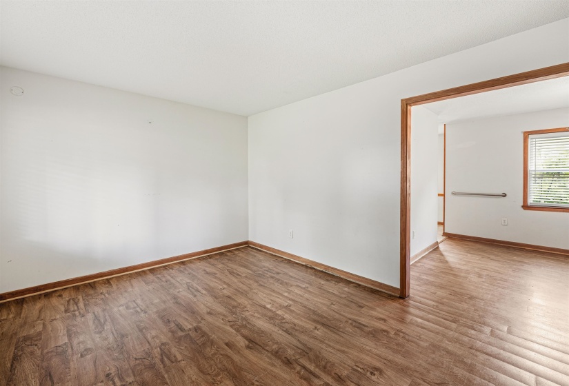 Spacious room featuring wood-finish flooring, white walls, and a wide entryway with wood trim