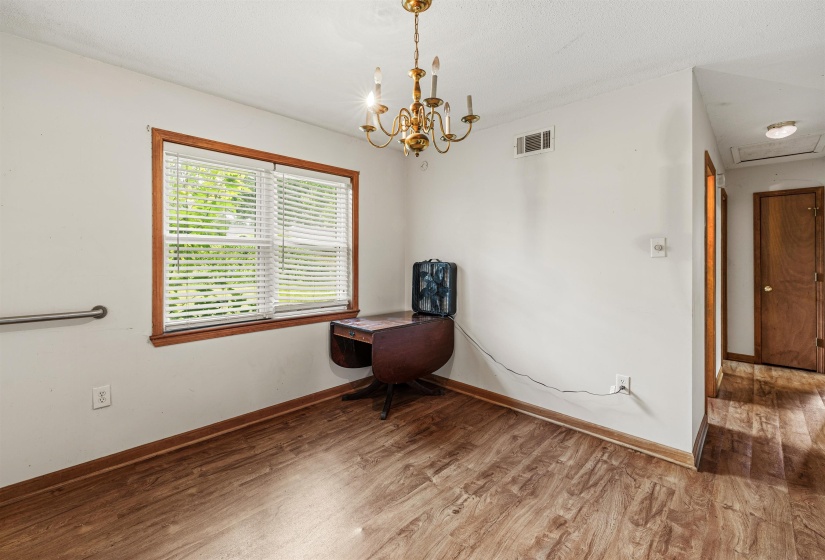 Interior space with wood-finish flooring, a brass chandelier, and a window featuring wood trim