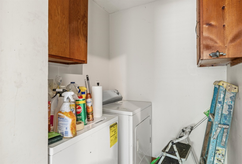 Laundry area featuring a side-by-side washer and dryer, wood-finish upper cabinetry, and white painted walls